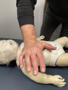 One‑hand infant CPR chest compressions on a baby manikin, demonstrating correct hand placement for AHA‑based CPR training in Atlanta for parents and caregivers.