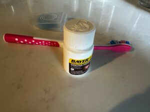 Bayer aspirin bottle on bathroom counter beside toothbrush and floss representing daily low dose aspirin heart health routine